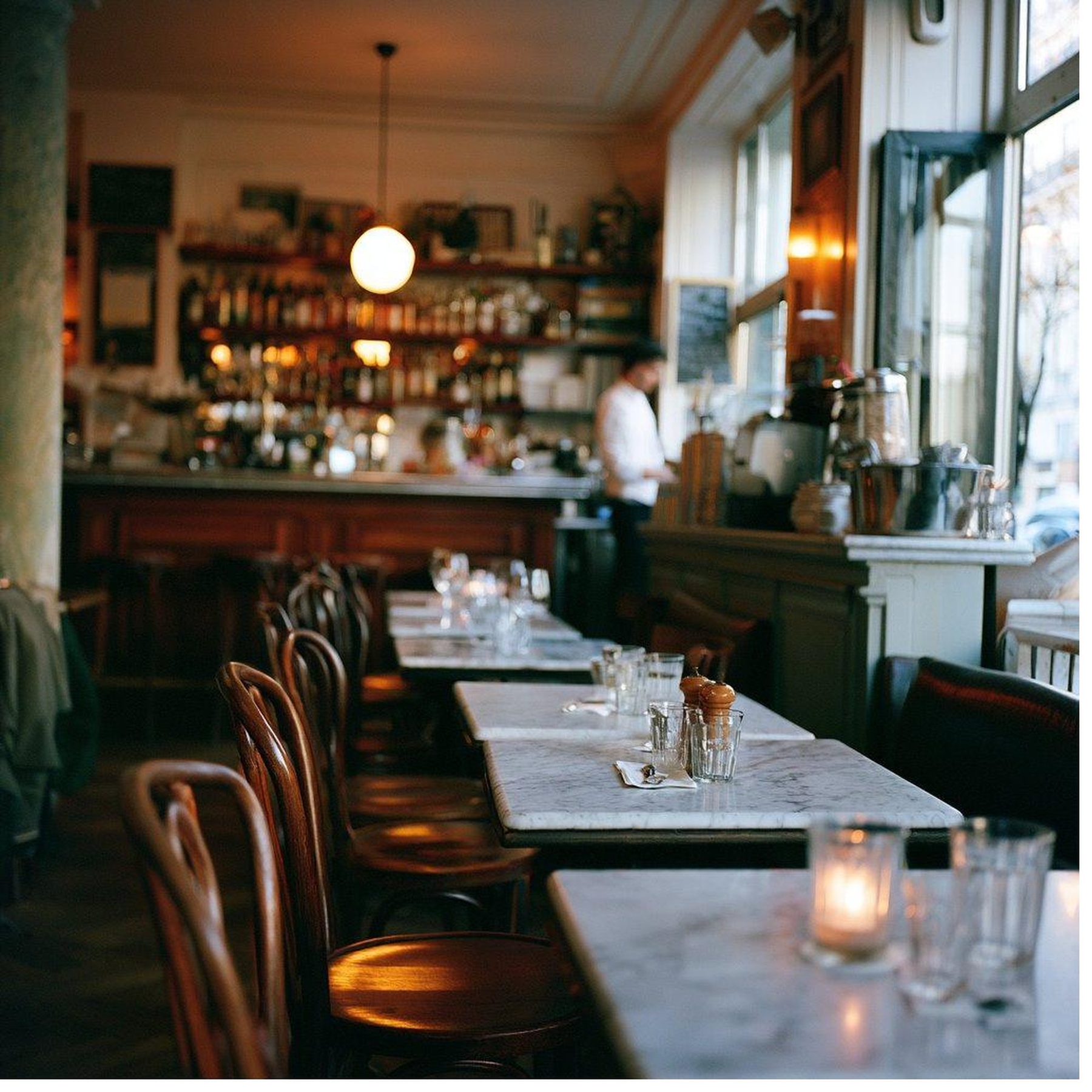 A dining room at evening service, the pass lit behind the room.