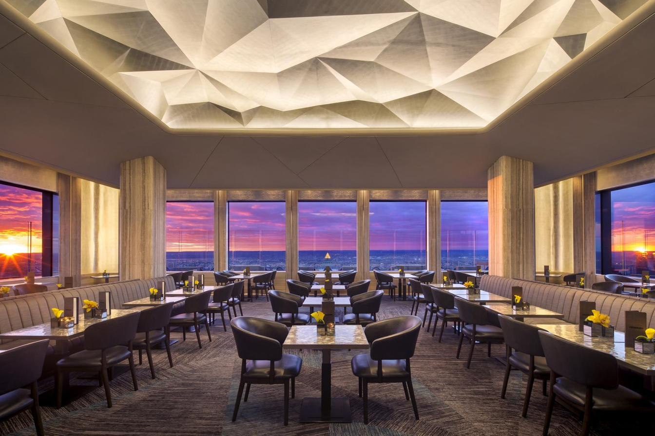 A dining room high above the city at sunset, the skyline burning through the windows.